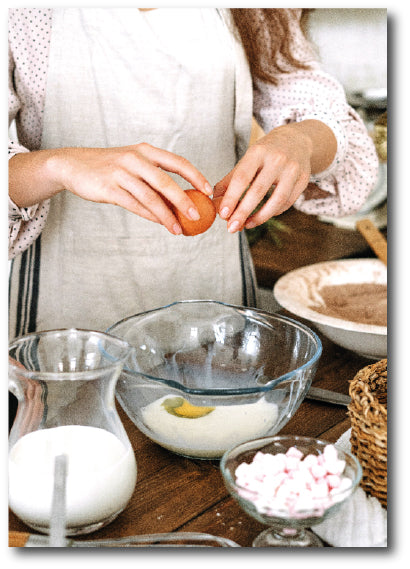 Dementia-friendly reminiscence artwork of a woman breaking eggs into a bowl alongside other products in her kitchen.  