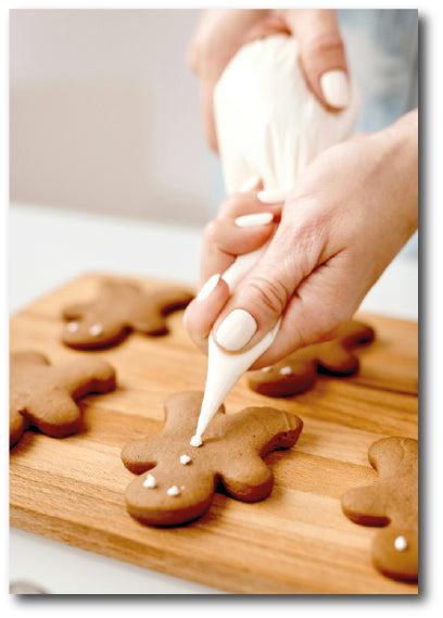 Dementia-friendly reminiscence image of baked gingerbread biscuits being iced by hand with a piping bag.